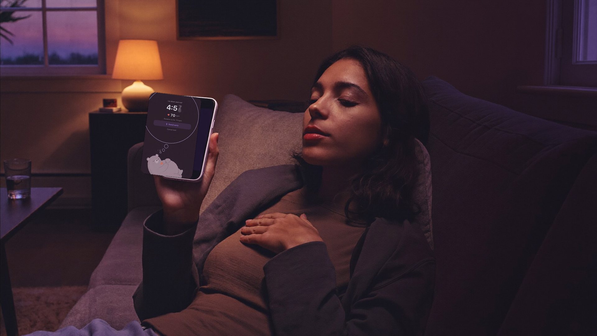 A woman resting on a sofa at dusk, checking a stand test on her phone